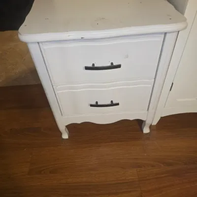 Sale Photo Thumbnail #32: White painted wooden nightstand featuring two drawers with modern black bar pull handles and cabriole legs in a French Provincial style. Top surface shows visible marks, scuffs, and signs of wear to the finish. Good candidate for refinishing or repainting