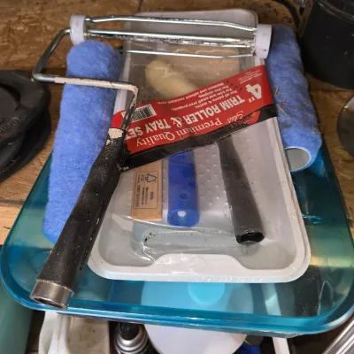 Sale Photo Thumbnail #182: Assorted painting supplies including standard paint roller frames, blue paint roller covers, a 4-inch trim roller & tray set in original packaging, and a plastic container.
