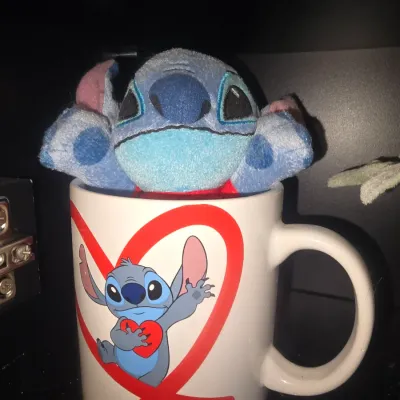 Sale Photo Thumbnail #21: Disney Lilo & Stitch ceramic mug featuring a graphic of Stitch holding a red heart inside a large heart outline, complete with a small matching plush Stitch figure inside. Good pre-owned condition with no visible chips or cracks on the mug.