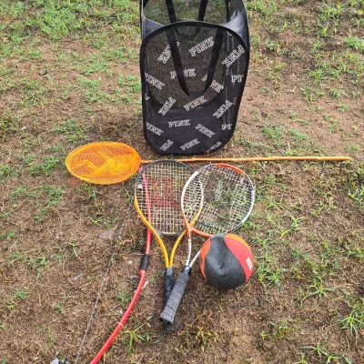 Sale Photo Thumbnail #154: An assortment of outdoor recreation and sports items including a Victoria's Secret PINK mesh pop-up hamper/bin, two tennis racquets, an orange long-handled fish/bug net, a small red bow, and an orange and black ball. All items show signs of outdoor use an