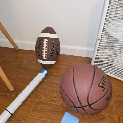 Sale Photo Thumbnail #184: Assorted sports gear lot including a Wilson NCAA football, a Spalding basketball, and a rolled Michael Jordan Chicago Bulls poster in its protective tube. Items show light wear consistent with use.