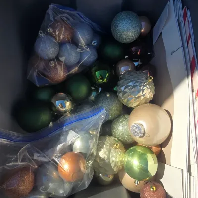 Sale Photo Thumbnail #124: A plastic tote filled with various Christmas tree ball ornaments in green, gold, silver, bronze, and glitter finishes. Includes both loose ornaments and bagged sets, featuring faceted, glittery, matte, and glossy finishes, along with additional paper gift