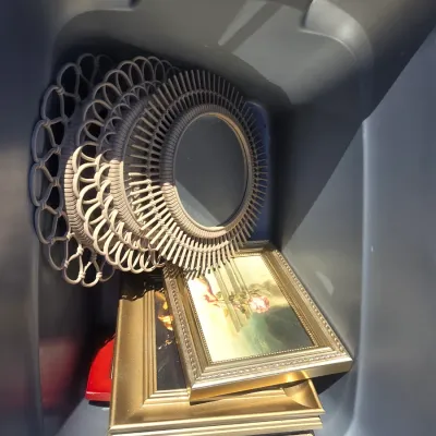 Sale Photo Thumbnail #108: Collection of various decorative wall artwork and photo frames including gilt-finished framed prints, ornate silver-tone and bronze-style tabletop frames, woven rattan/wicker style sunburst accent mirrors, and mosaic/textured picture frames. Plastic stora