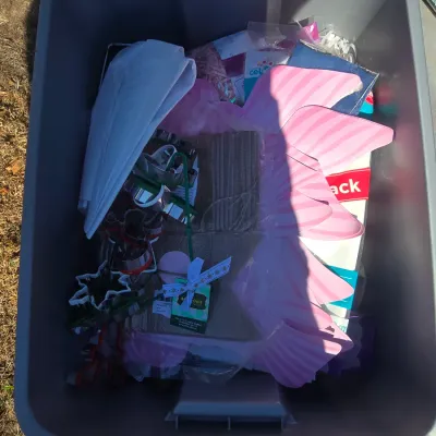 Sale Photo Thumbnail #119: Assortment of party and baking supplies stored in a plastic tote. Includes various metal cookie cutters, decorative gift bags, tissue/shredded paper, pink decorative items, small gift boxes, and related crafting or host accessories. Items appear unused or