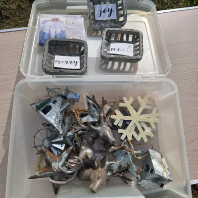 Sale Photo Thumbnail #166: An assortment of rustic and farmhouse-style Christmas decorations and ornaments inside a plastic storage tote. Includes rustic metal deer head ornaments, galvanized metal stars, windmills, barn motifs, a snowflake ornament, three small grey wooden baskets