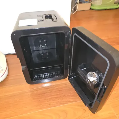 Sale Photo Thumbnail #205: Compact black and metallic finish Frigidaire mini fridge/cooler with a carrying handle on top. Features a removable inner shelf and a small door basket. Shows light surface dust and minor wear from use. Untested.