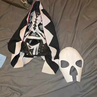 Sale Photo Thumbnail #191: Lot includes a black and white hooded Lucha Libre style professional/costume wrestling mask with sequin/glitter detail accents, along with a plain white molded plastic face mask shell. Both items appear to be in good pre-owned condition with light wear.