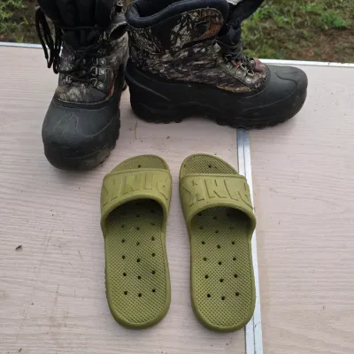 Sale Photo Thumbnail #158: Lot includes a pair of size 10Thermolite insulated camouflage hunting boots with rubber soles and lace-up tops, alongside a pair of olive green size 8 Victoria's Secret PINK slide sandals. Both pairs show light wear and use consistent with age.