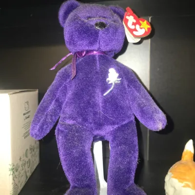 Sale Photo Thumbnail #19: Ty Beanie Babies Princess the Bear, issued in memory of Princess Diana. Features a rich purple plush body with an embroidered white rose on the chest and a matching purple neck ribbon. Original red heart-shaped Ty swing tag attached to the ear. Appears in