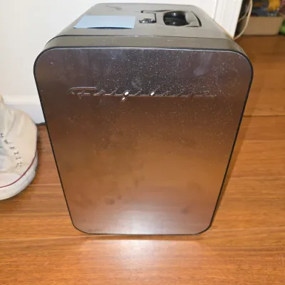 Sale Photo Thumbnail #206: Compact black and metallic finish Frigidaire mini fridge/cooler with a carrying handle on top. Features a removable inner shelf and a small door basket. Shows light surface dust and minor wear from use. Untested.