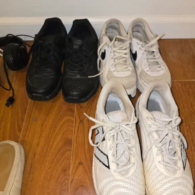 Sale Photo Thumbnail #202: Lot includes three pairs of size 8 athletic sneakers: one pair of black athletic shoes, one pair of white Nike sneakers, and one pair of white patterned athletic shoes. All pairs show visible signs of wear, scuffing, and dirt from use. Sizes are not clear