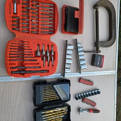 Sale Photo Thumbnail #156: An assortment of hand tools and power tool accessories. Includes two drill bit cases with driver bits and drill bits, socket sets on rails, a C-clamp, mini ratchet with driver bits, and various small hardware accessories. Items show typical signs of light