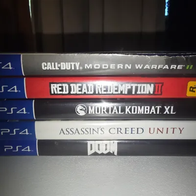 Sale Photo Thumbnail #64: Stack of 5 video games for the PlayStation 4 (PS4) console in original cases. Includes Call of Duty: Modern Warfare II, Red Dead Redemption II, Mortal Kombat XL, Assassin's Creed Unity, and Doom. Cases show minor shelf wear.