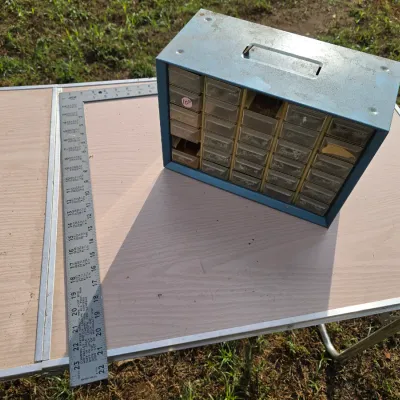 Sale Photo Thumbnail #161: Blue painted metal cabinet organizer with clear plastic drawers, ideal for hardware, small tools, or craft storage. Shows light surface wear, dust, and scuffing consistent with age and use. Measures approximately 10-11 inches wide.
