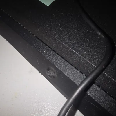 Sale Photo Thumbnail #60: Sony PlayStation 4 (PS4) Slim gaming console in matte black. Includes two DualShock 4 wireless controllers (one black, one purple) and connecting cables. Shows minor surface scuffs and signs of normal wear. Small melt spot