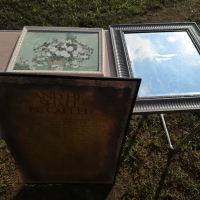 Sale Photo Thumbnail #178: Collection of framed wall art and decor including a framed floral print after Van Gogh's 'Roses', a dark ribbed framed wall mirror, and a framed religious text print titled 'And He Shall Be Called...'. Items show light surface wear and minor dust from han