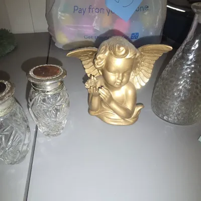 Sale Photo Thumbnail #77: Collection of decorative tabletop items including a gold-tone cherub/angel figurine holding flowers, two cut glass shakers with silver-tone caps, and a textured clear glass decanter or bottle with a stopper. Shows some wear, tarnish on metal caps, and sur