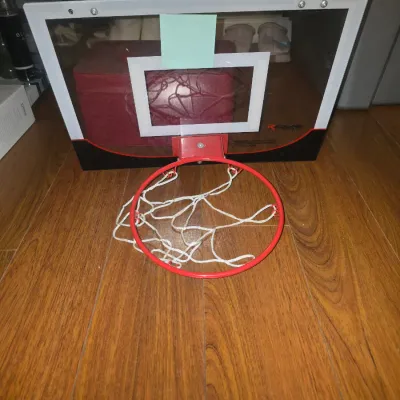 Sale Photo Thumbnail #48: Mini basketball backboard and hoop featuring a clear plastic backboard with white graphics, a red metal rim, and attached white netting. Ideal for bedroom or office door mounting. Appears gently used in good condition. Ball not included.