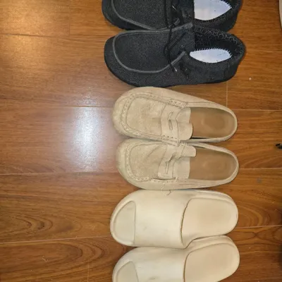 Sale Photo Thumbnail #201: Lot includes three pairs of men's size 8 casual footwear: one pair of dark grey canvas lace-up slip-on shoes (Hey Dude style), one pair of tan suede penny loafer slip-ons, and one pair of off-white foam slide sandals. Items show light to moderate wear on 