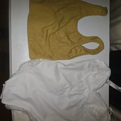 Sale Photo Thumbnail #82: Assorted lot of women's apparel including tank tops, cropped tops, knit sweater vests (including checkered patterns and 'miss love' brand), a pink tiered ruffle top, a white lace-trimmed bodysuit, a gold crop top, and knit socks. Items are lightly used to