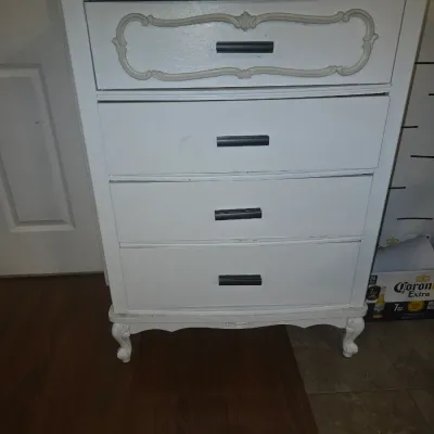 Sale Photo Thumbnail #29: Four-drawer wooden dresser painted white with French Provincial style cabriole legs and molding details on the top drawer front. Features modern black bar pull handles. Shows some light wear, scuffs, and paint imperfections consistent with use and repaint