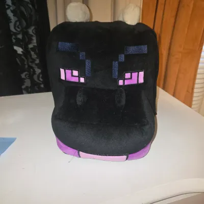Sale Photo Thumbnail #66: Black plush Minecraft Ender Dragon backpack featuring pixelated purple eyes, snout, and small horns. Soft fabric exterior, lightly used with minor wear visible.