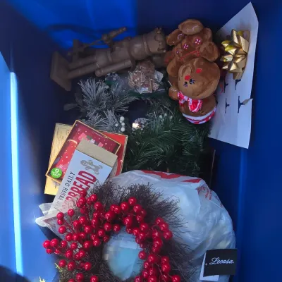 Sale Photo Thumbnail #126: Large collection of Christmas decorations contained in a blue plastic storage tote. Includes red berry wreaths, artificial greenery, a plush gingerbread figure, wooden nutcracker, gingerbread signage, gift bows, and decorative accents. Items appear to be 