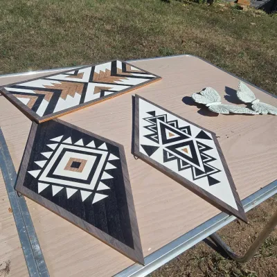 Sale Photo Thumbnail #147: A set of decorative wall art pieces including three geometric wooden panels featuring Southwestern style painted designs in black, white, and natural wood tones. Also includes two white butterfly wall decorations. In good pre-owned condition with light we