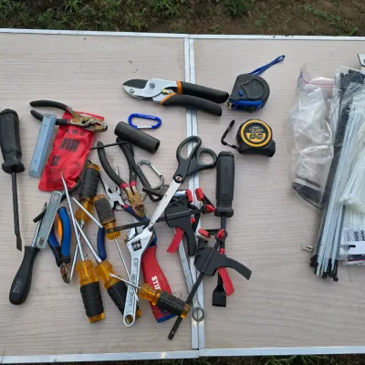 Sale Photo Thumbnail #155: An assortment of household hand tools including various screwdrivers, pliers, wire cutters, small bar clamps, scissors, tape measures, pruning shears, an adjustable wrench, carabiners, and packages of nylon cable ties. Items show varying signs of wear, su