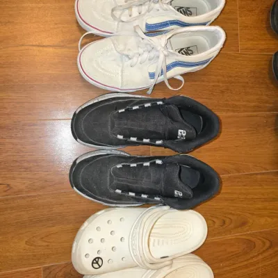 Sale Photo Thumbnail #203: Lot of 3 pairs of shoes including: size 8
- Vans off-white canvas/suede low-top sneakers with blue sidestripe details
- Jordan Brand black laceless mid-top sneakers
- Off-white Crocs foam clogs with peace sign Jibbitz charm

All shoes show pre-owned wear 