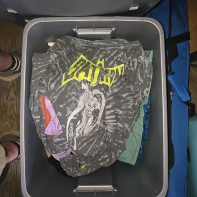 Sale Photo Thumbnail #128: Storage tote filled with an assortment of casual clothing including a Batman tie-dye graphic long-sleeve top, knits, sweaters, tops, and button-up shirts in various colors. Items show light wear consistent with gentle use.