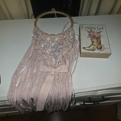 Sale Photo Thumbnail #70: Lot of 2 Western/Rustic themed decor pieces, including:
- Handcrafted pink macrame fringe wall hanging attached to a wooden hoop with bow accent.
- Wooden block sign featuring 'Country Girl' text with cowboy boot, flowers, and horseshoe graphics.

Both it