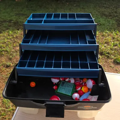 Sale Photo Thumbnail #165: Flambeau Outdoors hard plastic tackle box featuring three blue fold-out cantilever trays with segmented compartments. Bottom storage area contains a collection of red and white fishing bobbers, floating lures, and small accessory cases. In good, usable co