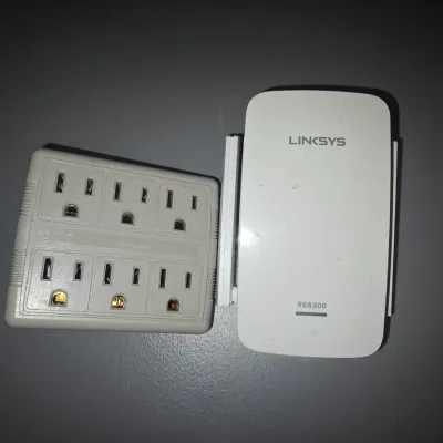 Sale Photo Thumbnail #74: Includes a Linksys AC750 BOOST Wi-Fi Range Extender (Model RE6300) with fold-out antennas and a white plastic 6-outlet grounding wall tap power expander. Both items show light wear from previous use.