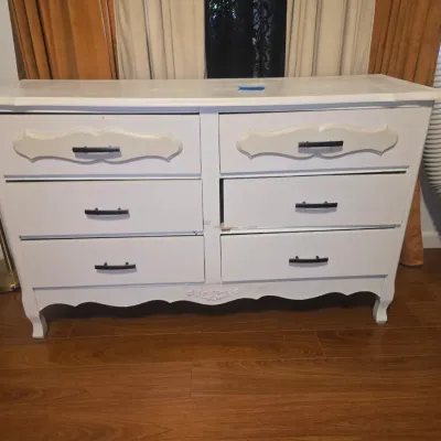 Sale Photo Thumbnail #10: White painted wooden 6-drawer dresser featuring French Provincial style molded accents and a scalloped bottom apron. Equipped with dark metal drawer pulls. Shows minor surface wear, scuffs, and paint marks consistent with use. 31x50x18