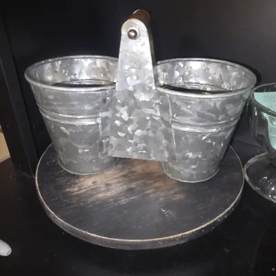 Sale Photo Thumbnail #24: Galvanized metal double bucket caddy featuring a center carrying bracket with a wooden handle grip. Rustic farmhouse style, suitable for utensil organization, condiments, or small planter display. Light cosmetic wear consistent with use. Includes lazy sus