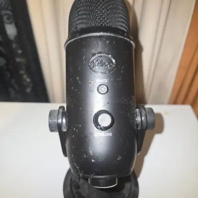 Sale Photo Thumbnail #79: A Blue Yeti USB condenser microphone in matte black finish, mounted on its original desktop stand. Features front controls for Mute and Headphone Volume. Item shows visible dust, spotting, and surface wear from prior use; untested. No cords