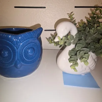 Sale Photo Thumbnail #30: A pair of ceramic decorative animal planters. Includes one glossy blue embossed owl planter and one white glazed swan planter containing faux greenery. Both items appear to be in good condition with no visible chips or cracks.