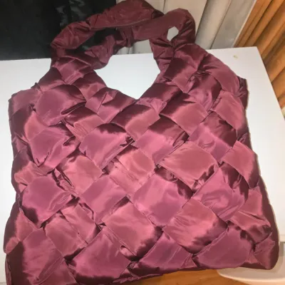 Sale Photo Thumbnail #87: woven puffer shoulder bag or tote in a burgundy/plum satin-finish fabric. Features a thick woven design on the exterior and an interior zip pocket with brand tag. Appears to be gently used with no major wear or damage visible.