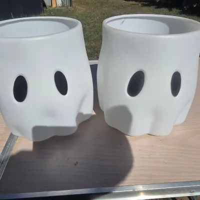 Sale Photo Thumbnail #138: A pair of white plastic ghost-shaped buckets or planters with simple black eyes. Ideal for Halloween decor, trick-or-treating, or seasonal display. Good condition with light surface wear.