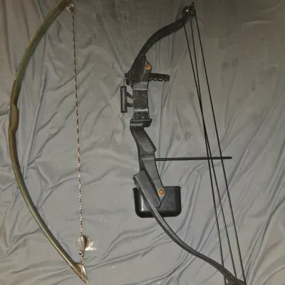 Sale Photo Thumbnail #192: Pair of youth archery bows, including one black compound bow equipped with a quiver/sight attachment and one traditional style recurve bow with a braided string. Both show signs of age, wear, and minor surface rust on metal hardware. Strings and cables ar