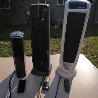 Sale Photo Thumbnail #171: A collection of three Lasko electric ceramic tower heaters in varying sizes (two black, one silver/white). Showing light surface wear consistent with standard use; functionality untested.