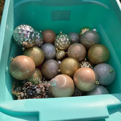 Sale Photo Thumbnail #174: Collection of holiday decorations including a plastic tote filled with modern shatterproof and metallic Christmas baubles in gold, silver, champagne, and blush tones, as well as pinecone accents. Also includes a white knit Victoria's Secret 'PINK' Christm