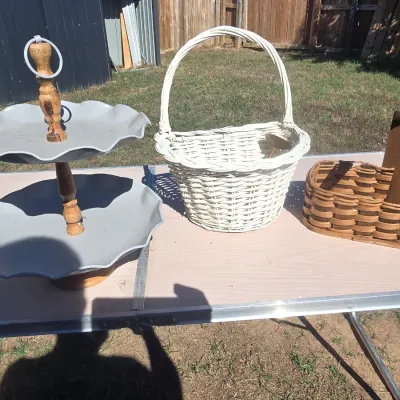 Sale Photo Thumbnail #141: A 3-piece lot featuring a two-tiered gray metal serving stand with turned wood center spindle, a white painted woven wicker basket with a high handle, and a natural brown woven splint wood caddy/basket with a fixed wooden handle. All items show minor surf