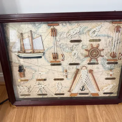 Sale Photo Thumbnail #44: Framed nautical shadow box featuring a world map background, small sailboat model, ship's wheel, anchor, and labeled knot tie displays.