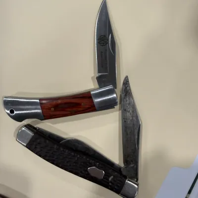 Sale Photo Thumbnail #415: Two vintage folding pocket knives, including an NRA National Rifle Association lockback knife with wood handle scales and a multi-blade knife with a textured dark handle.