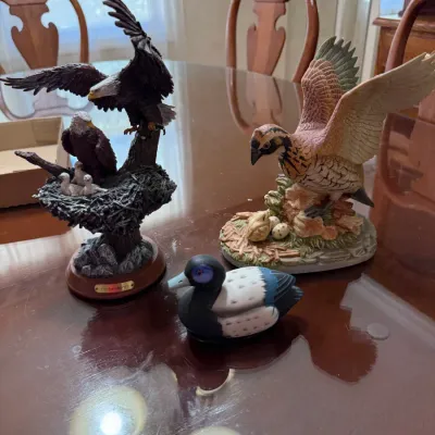 Sale Photo Thumbnail #251: Collection of three bird figurines displayed on a dining table, including a bald eagle family sculpture, a game bird with wings spread, and a small duck decoy.