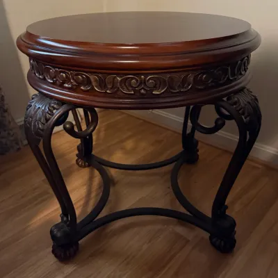 Sale Photo Thumbnail #80: Round wood and metal accent table featuring a carved apron with scroll detailing and ornate wrought metal legs.