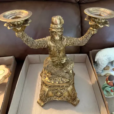 Sale Photo Thumbnail #337: Vintage gold-toned monkey candlestick holder featuring a monkey in a vest and hat holding two candle sockets.