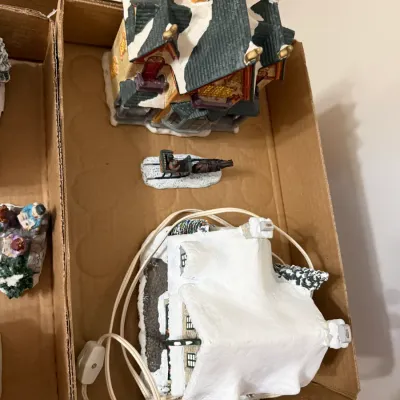Sale Photo Thumbnail #354: Collection of illuminated ceramic Christmas village buildings and a horse-drawn sleigh figurine stored in cardboard boxes.